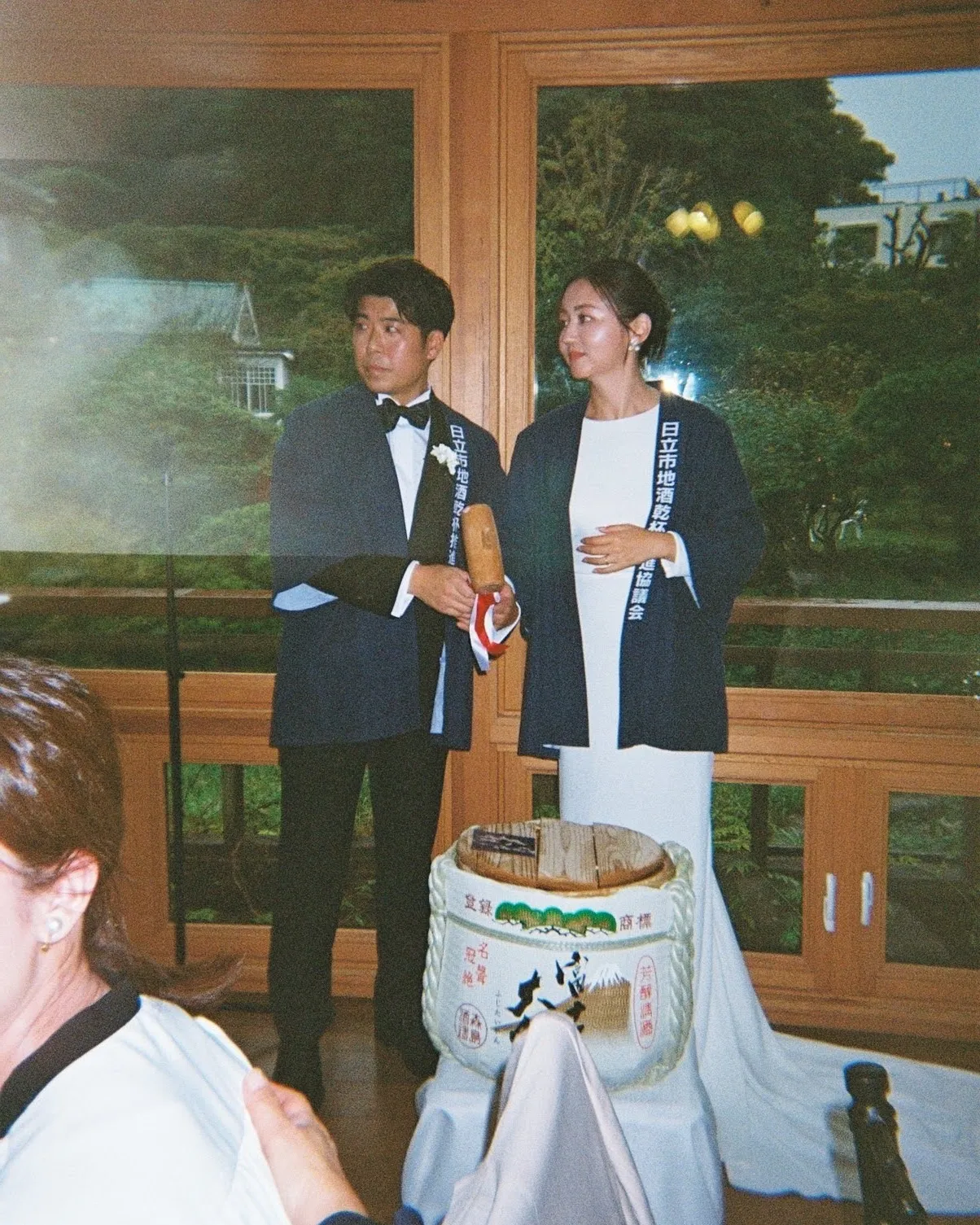 法被を羽織って酒樽の前に立つ新郎新婦（S夫妻）